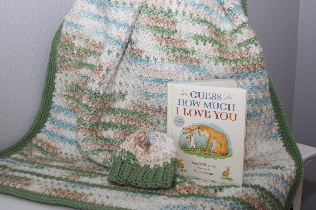 warm woodlands themed baby blanket draped over a basket with a hat and book

