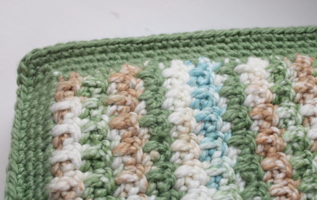Warm woodlands themed baby blanket in green, blue, ivory, and brown showing the border and stitches