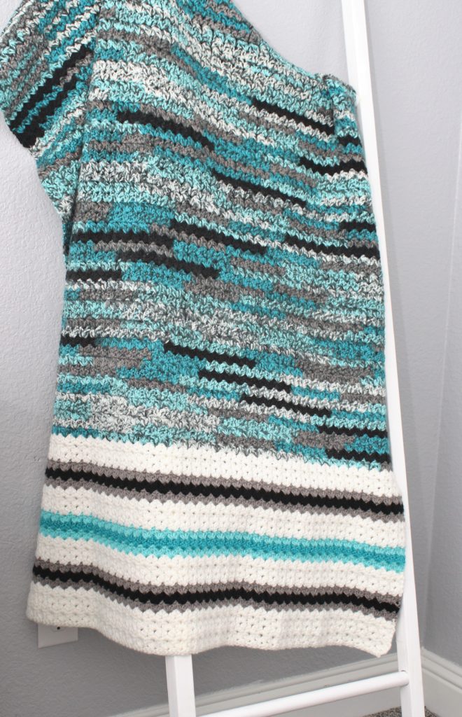 Beautiful and colorful cluster v-stitch throw in grey, teal, white, and black, draped over a blanket ladder.