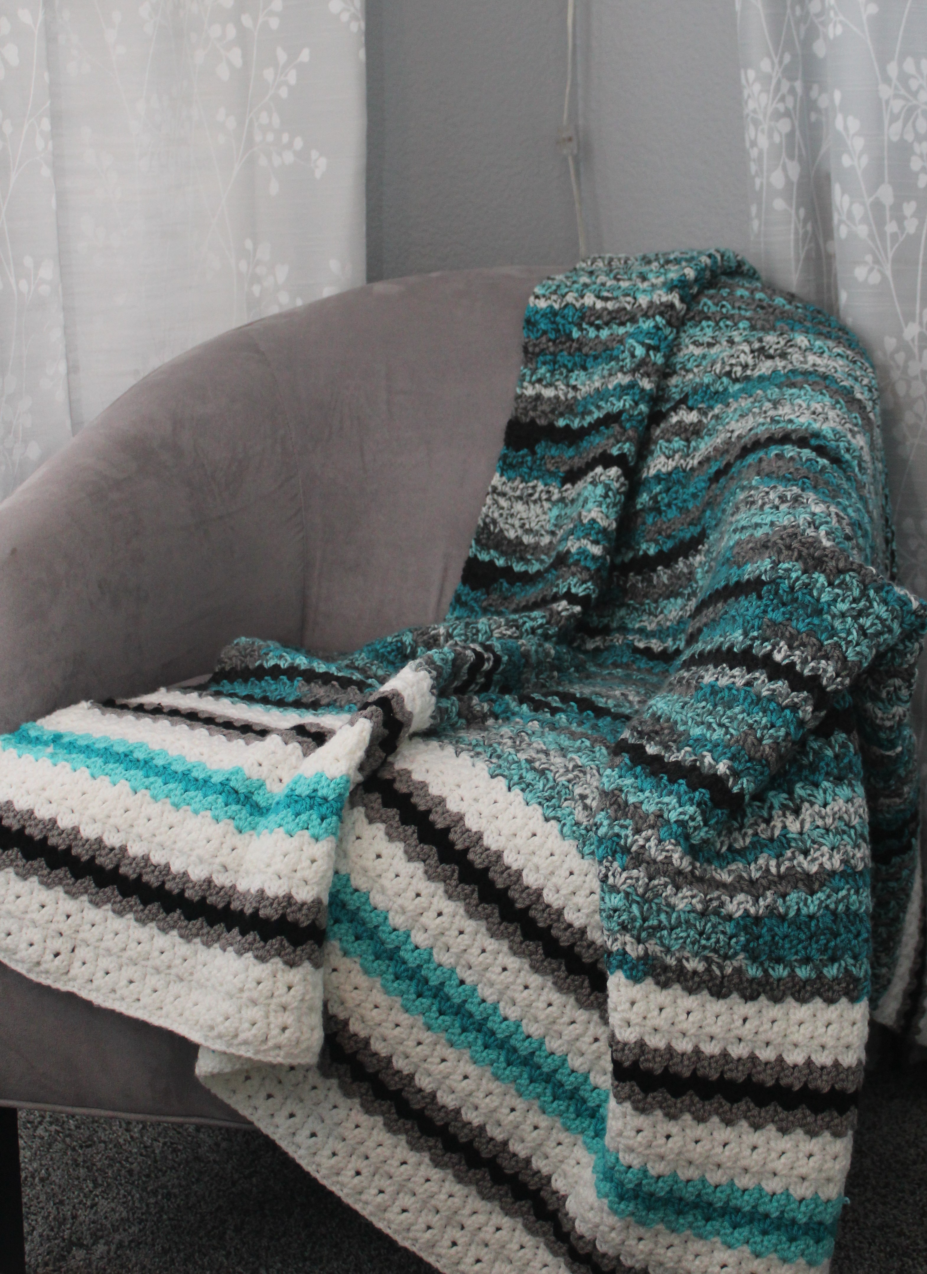 teal, black, grey, and white afghan draped over chair in corner next to window