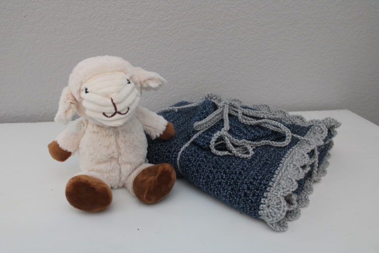 navy and silver baby blanket folded on a dresser with toy lamb