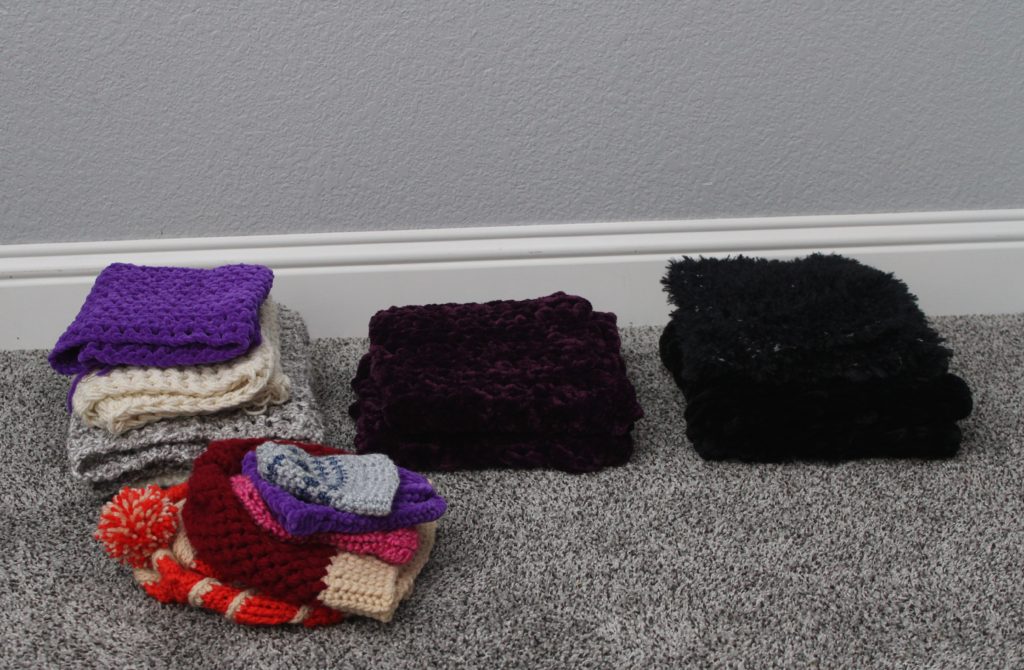 sorted piles of crocheted scarves and hats