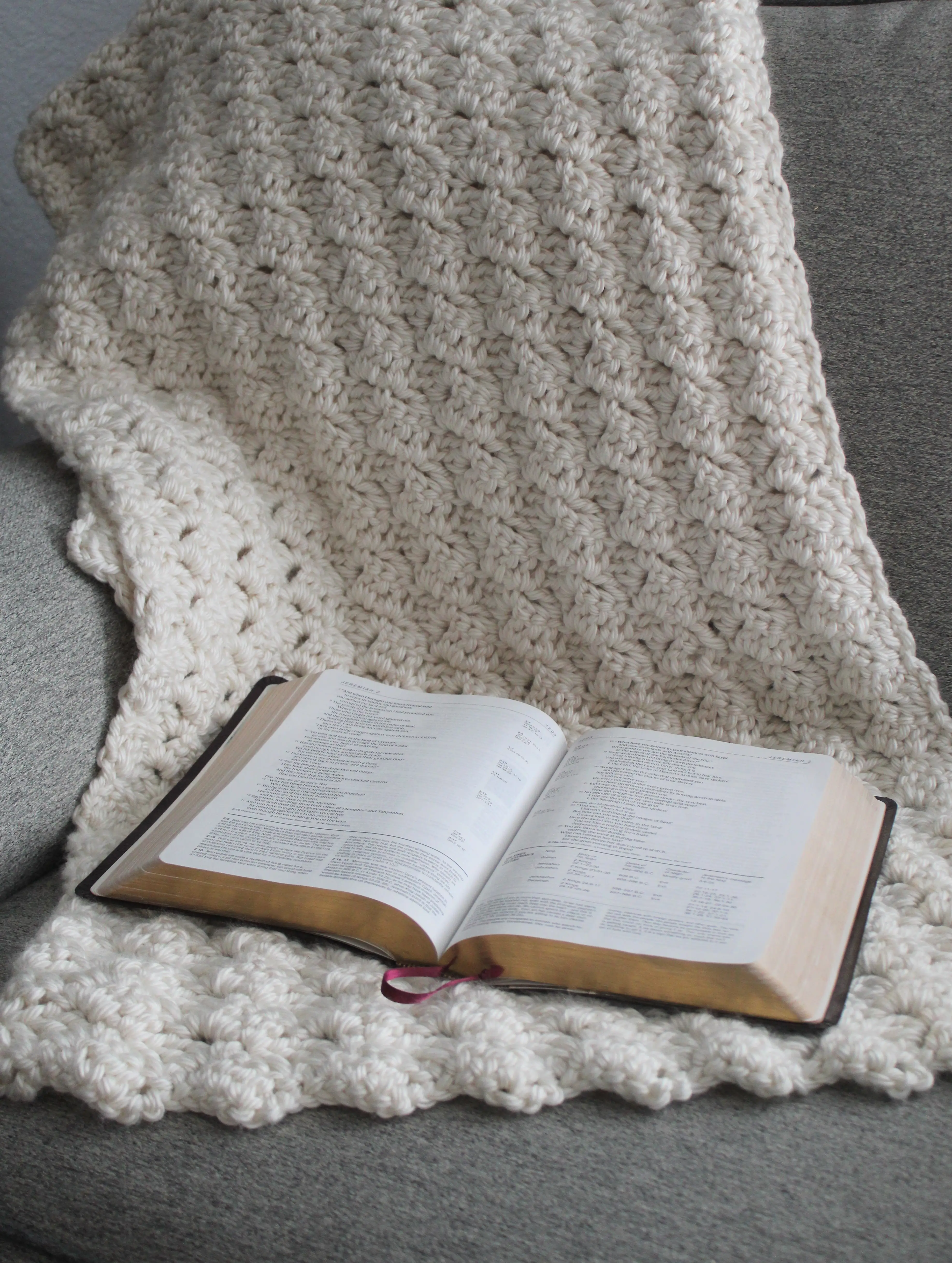 Slanted double crochet shawl in ivory crocheted shawl draped over a grey chair and an open bible on the shawl