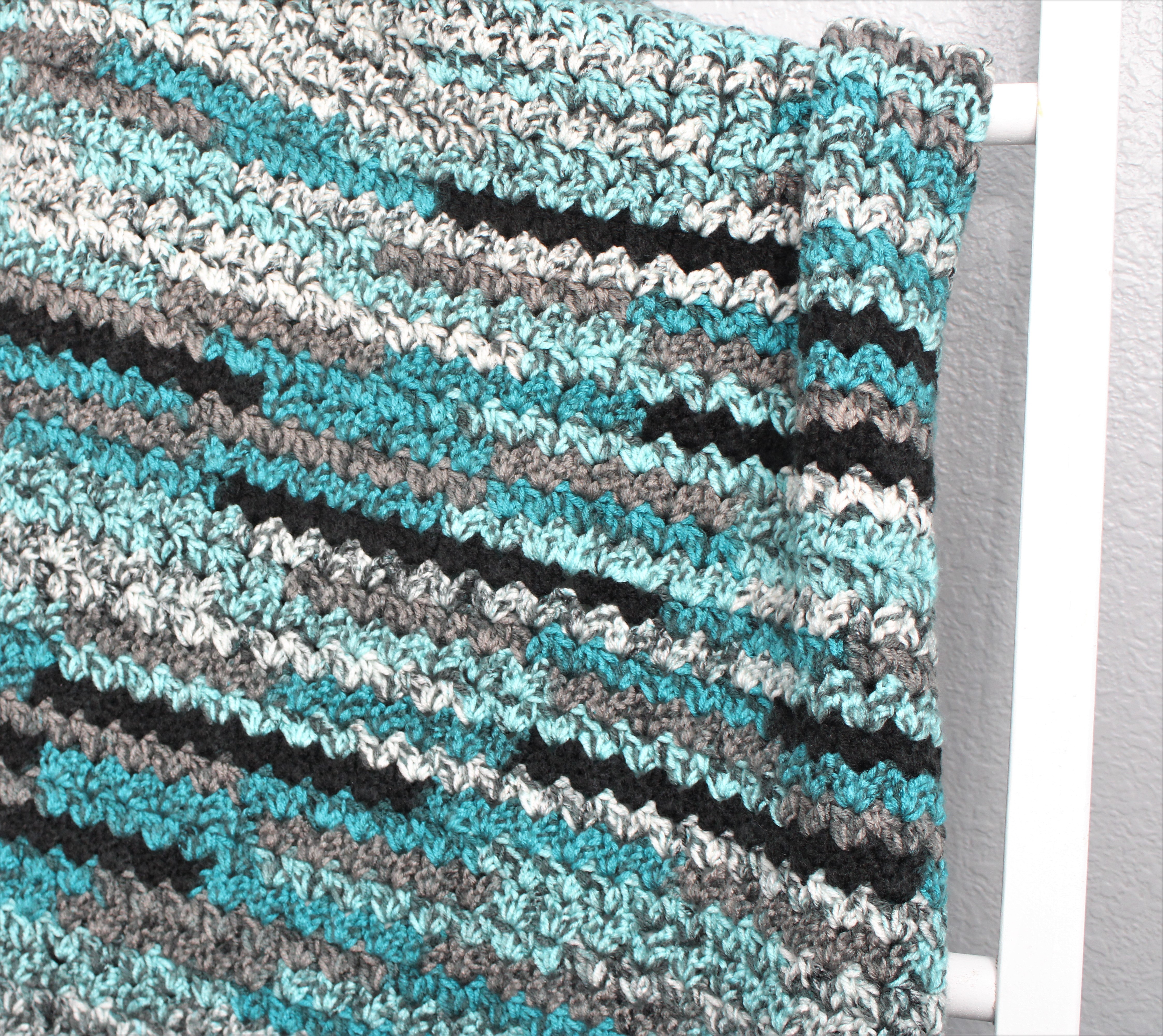 up close view of teal, black, white and grey afghan on a rack