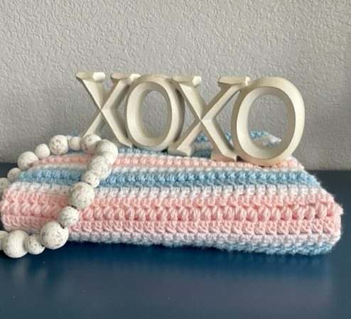 pink, blue and white folded baby afghan with xoxo and beads on it