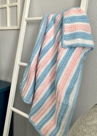 Pink, Blue, and white baby afghan draped over a blanket ladder