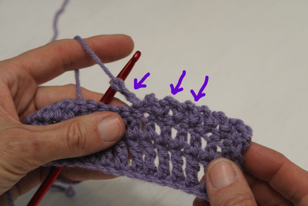 hands holding purple yarn showing a chain of texture