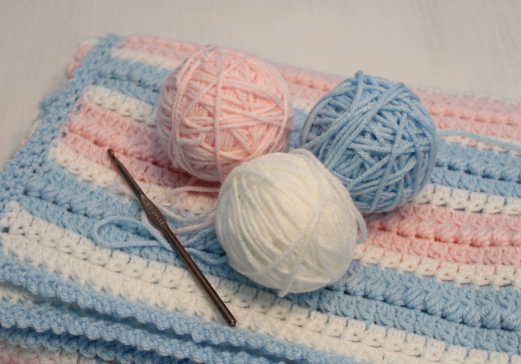 cotton candy puff blanket in pink, blue, and white balls of yarn on top of folded afghan