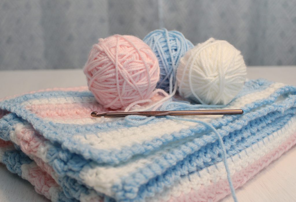 Cotton Candy puff blnaket in blue, white and pink balls of yarn on top of folded afghan with hook