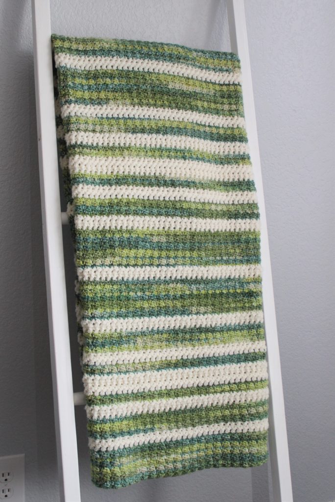green and ivory striped afghan folded and draped over a throw ladder