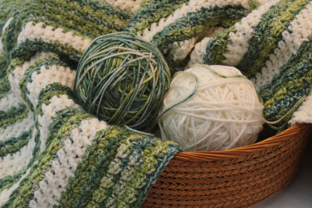 green and ivory balls of yarn in a basket with Wintergreen Crochet Throw