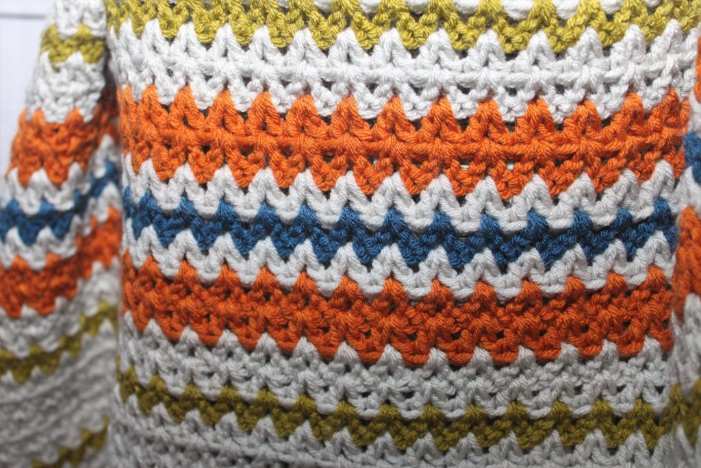 close up of the stitches of an orange, grey, green and blue afghan
