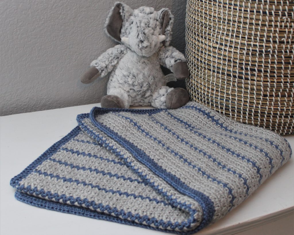 grey and blue striped afghan folded in front of a basket and elephant toy