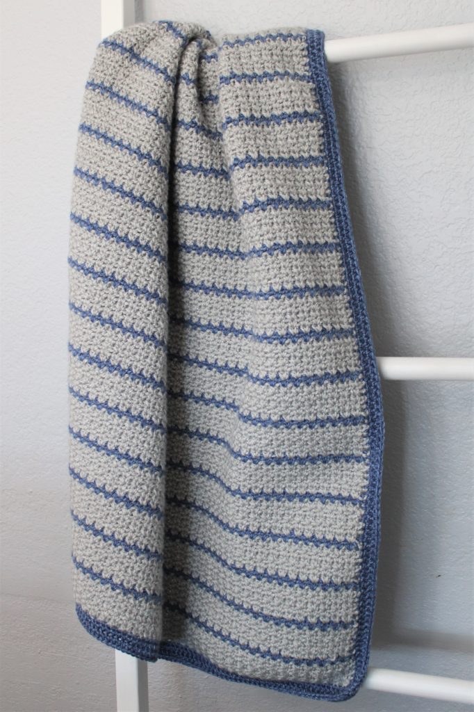 grey and blue striped afghan draped on a blanket ladder