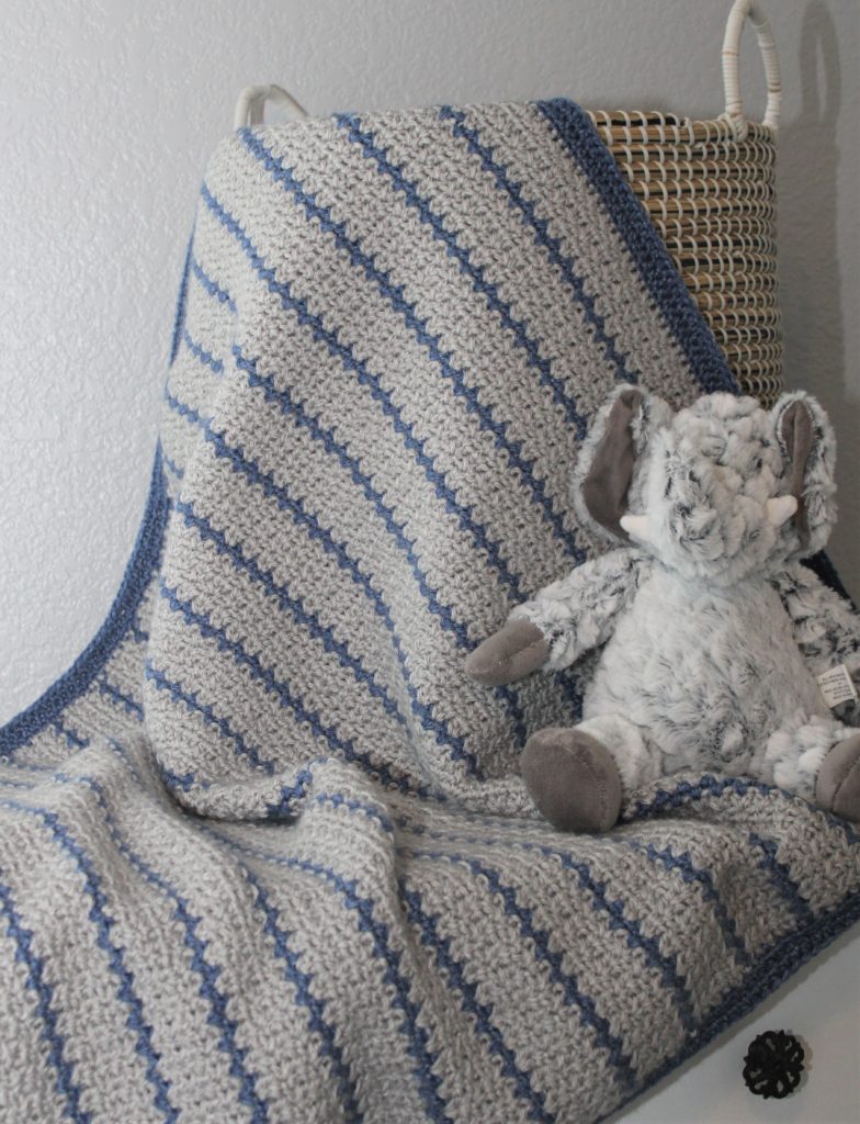 MOdern Striped HDC v-stitch afghan in grey and blue striped crocheted afghan draped in basket with elephant