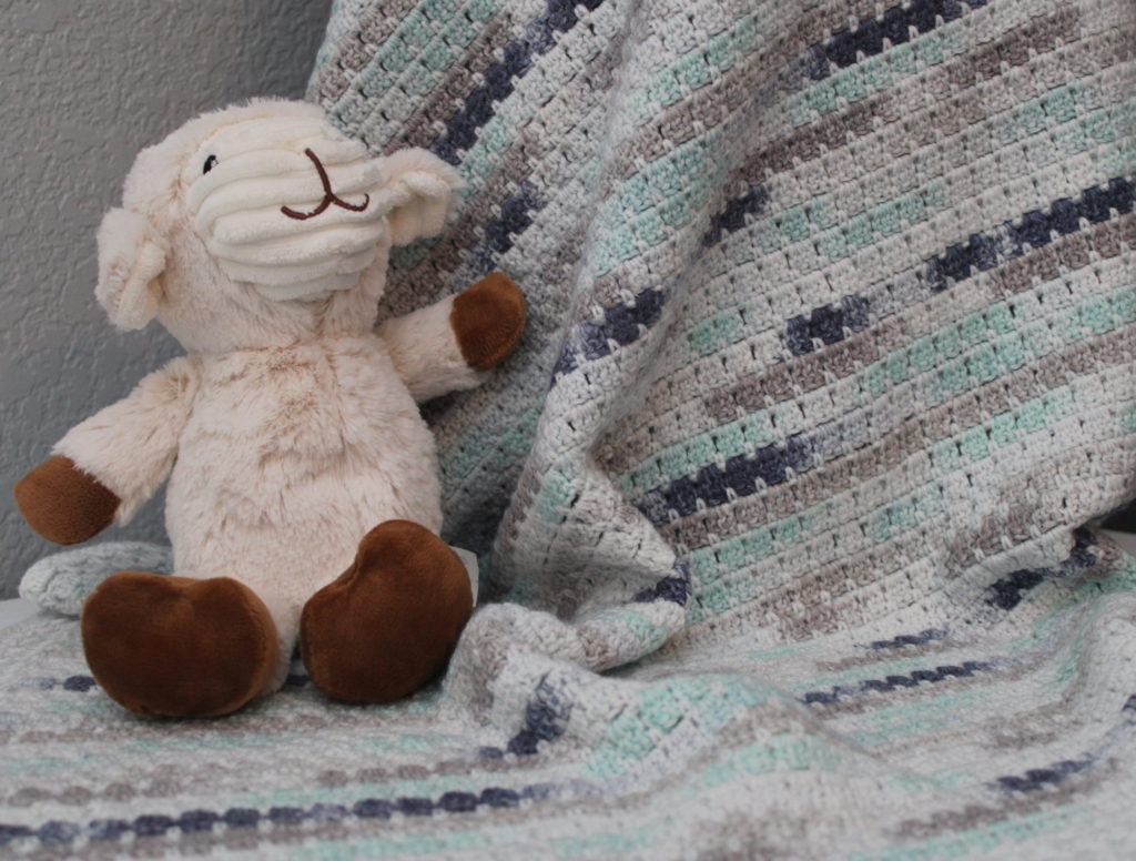 Little Boy Blule Block in Blue, green, white crocheted block stitch blanket draped over a basket with a bunny