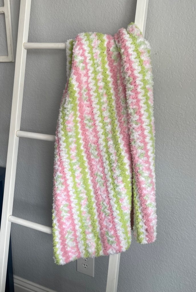 pink, green, and white striped baby afghan hanging on a blanket ladder