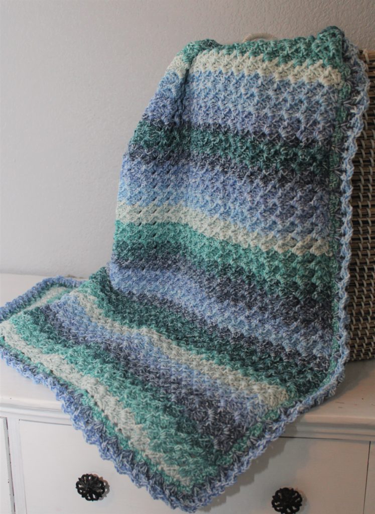 afghan draped over a basket in blues, and greens