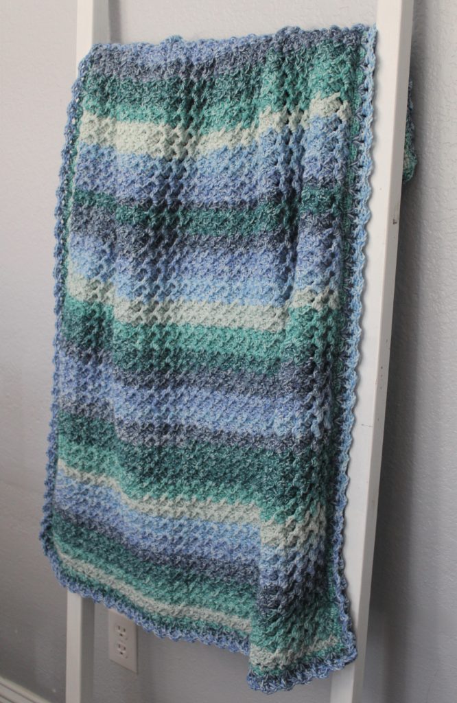 Seashore by Moonlight baby afghan in blues and greens hanging on a white blanket ladder