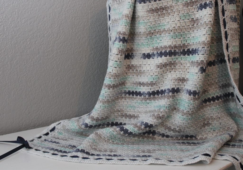 blue, grey and whtie black stitch afghan draped over basket