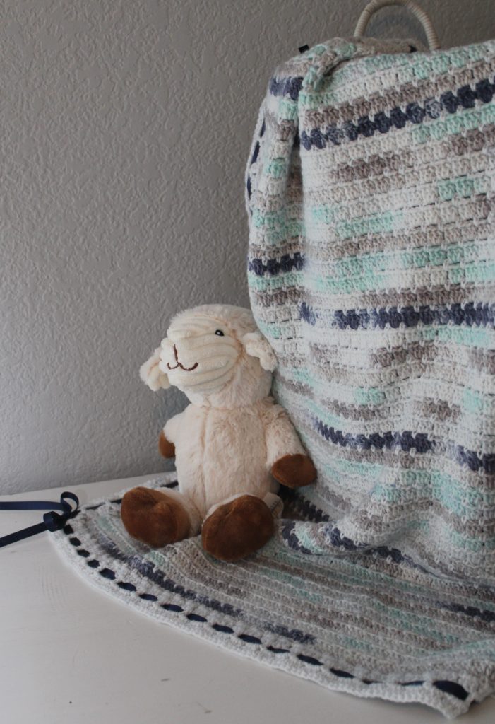 baby afghan in blues and greys draped over a basket with a lamb