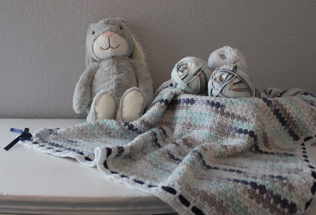 blue and grey baby blanket draped over basket with grey bunny