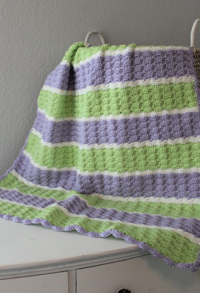 green, purple, and white striped afghan draped over a basket