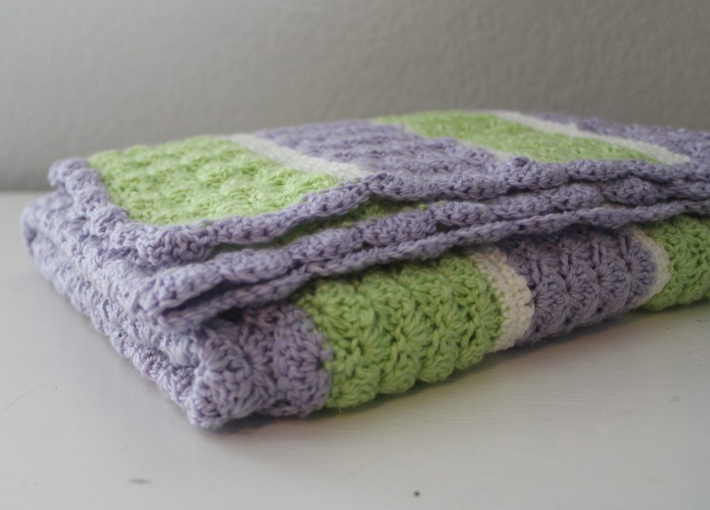green purple and white striped afghan folded on a dresser