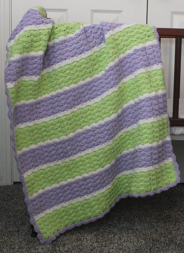 green, purple, and white shell stitch blanket draped over a crib