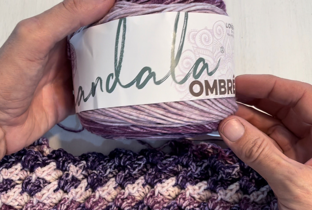 hands holding a cake of yarn in purple used in Love's embrace Prayer shawl.