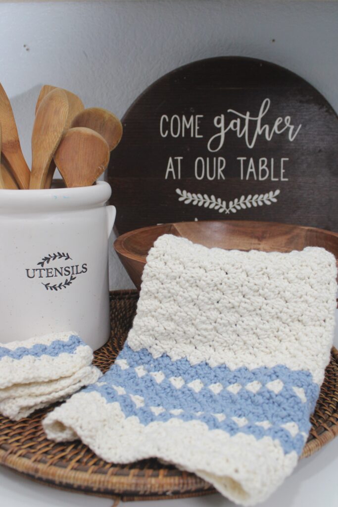 Sedge stitch farnhouse tea towel set in blue and white towel draped in a bowl sitting next to a kitchen utensil can with wooden spoons in it. A tray sits behind the bowl