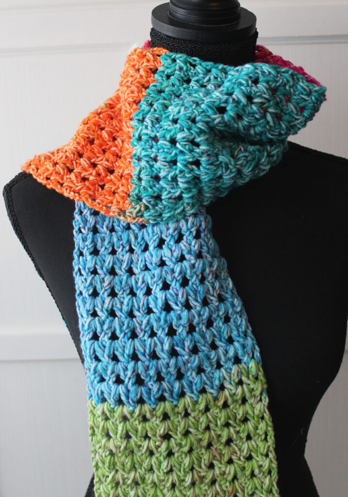 The Happy scarf, a forked cluster stitch draped over a manequine in bright colors of blue, orange and pink.
