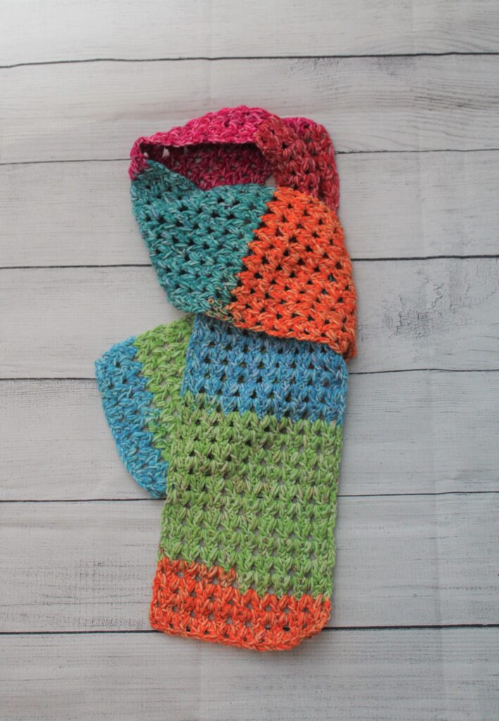 The happy scarf in bright colored crocheted scarf folded and laying on shiplap