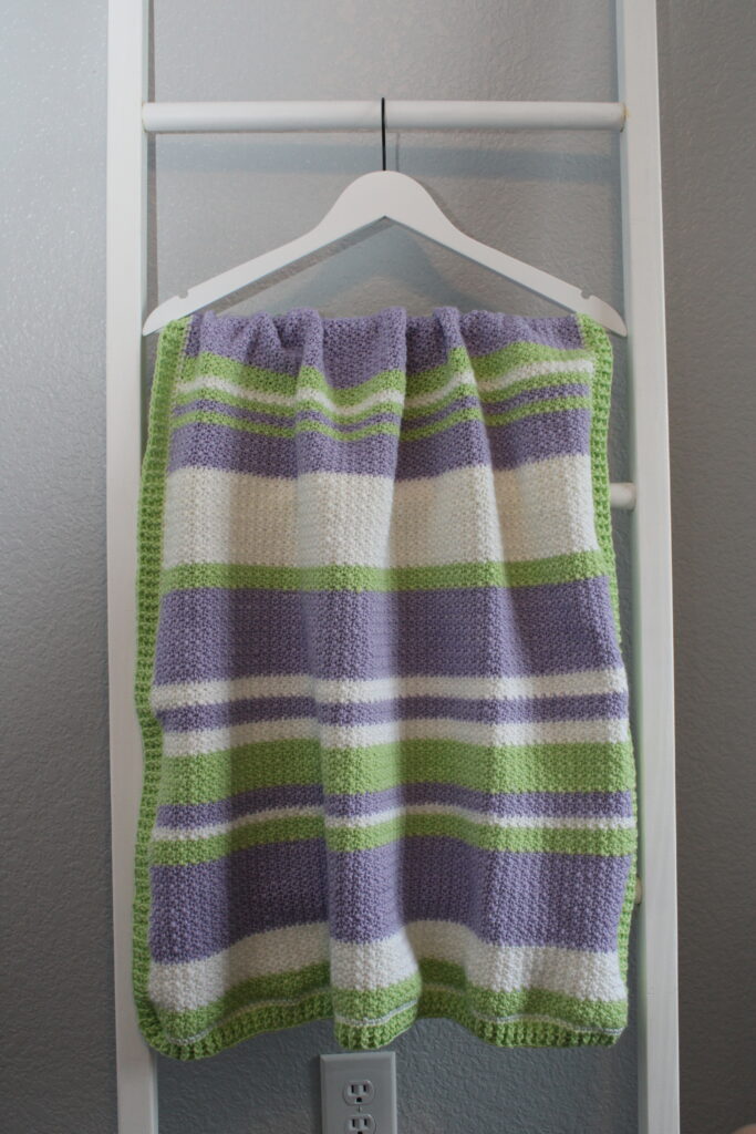 Delightful Springtime Modern Stripe blanket hanging on a blanket ladder in purple, green, and white.