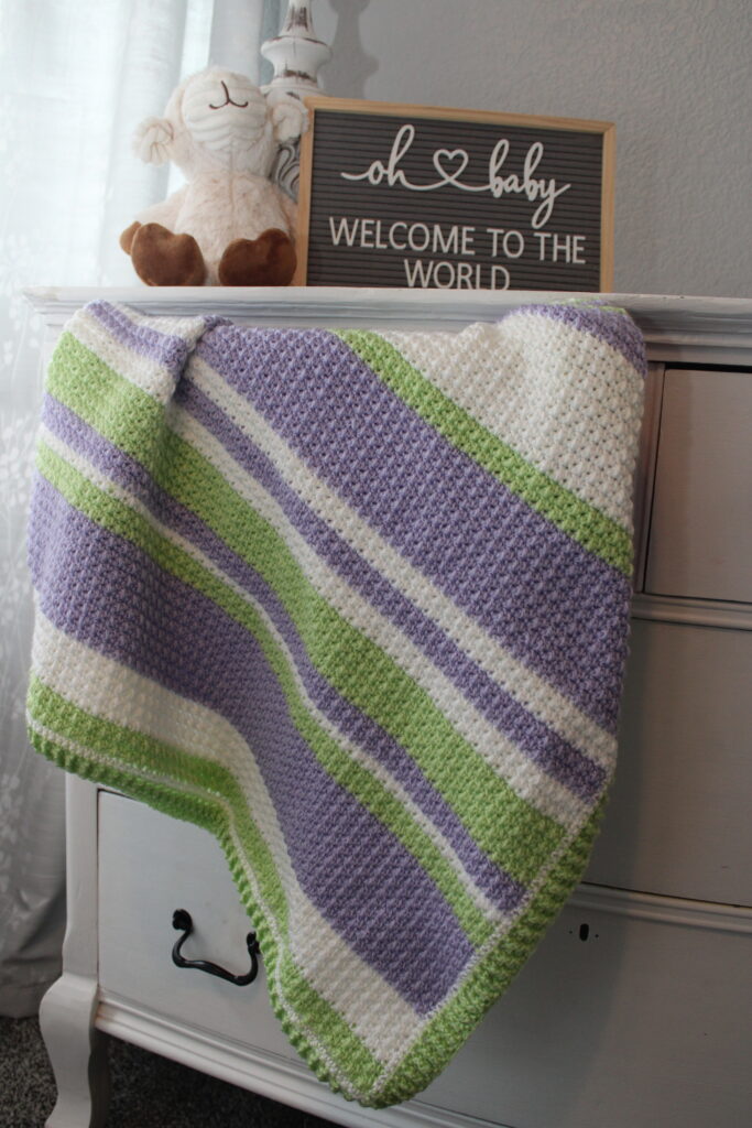 Delightful Springtime Modern Stripe Baby Blanket draped out of a dresser drawer in purple green and white stripes
