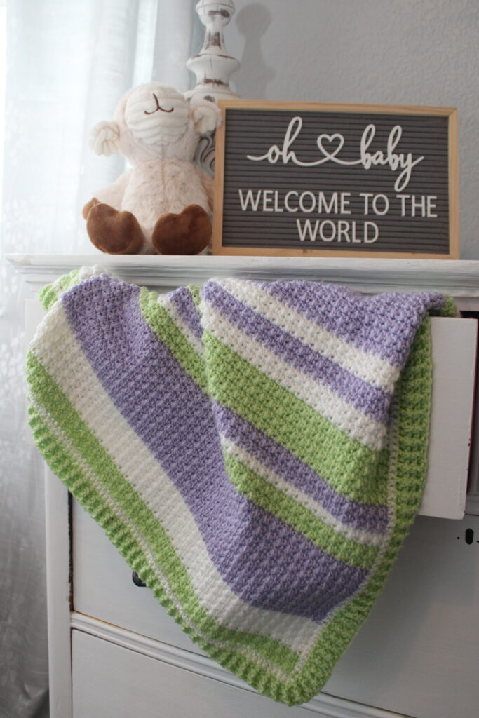 Delightful Springtime blanket hanging out of a dresser drawer in purple, green, and white.