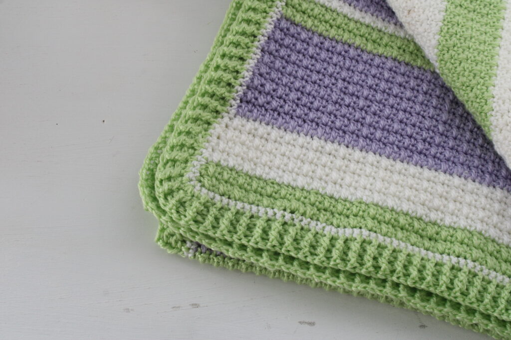 Delightful Springtime blanket folded and showing up close of the border in green, white, and purple.