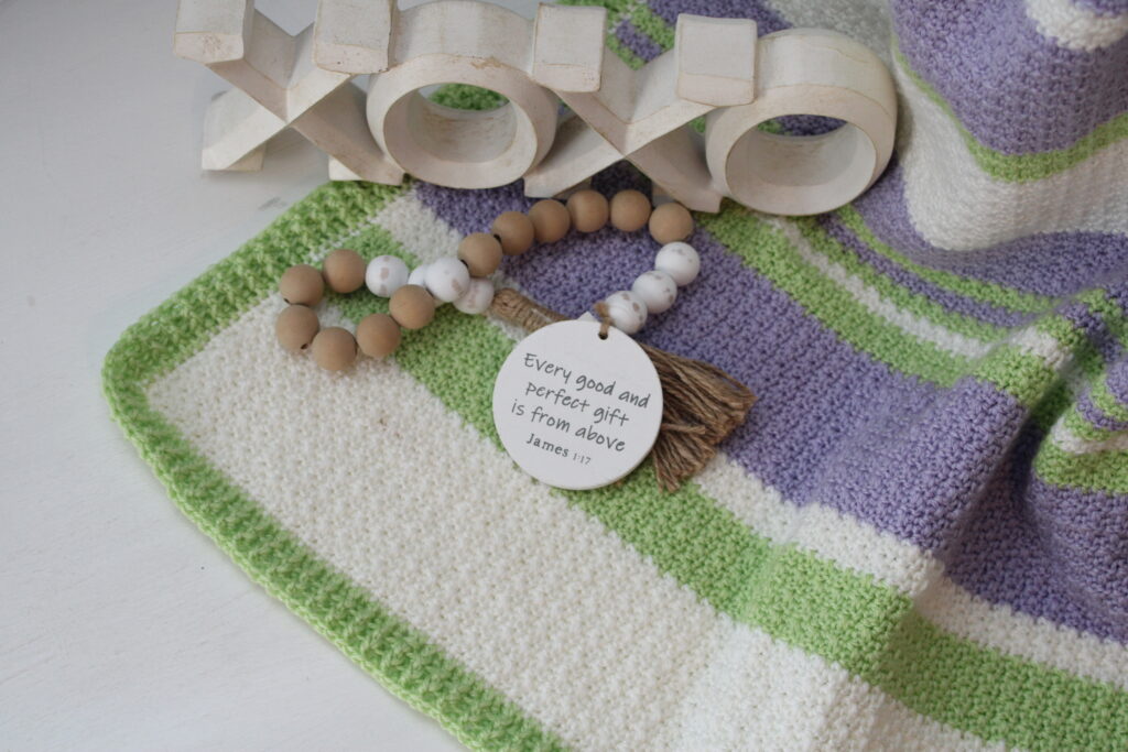 Delightful Springtime blanket pictured from above with beads and xoxoxo figure in purple, green, and white.