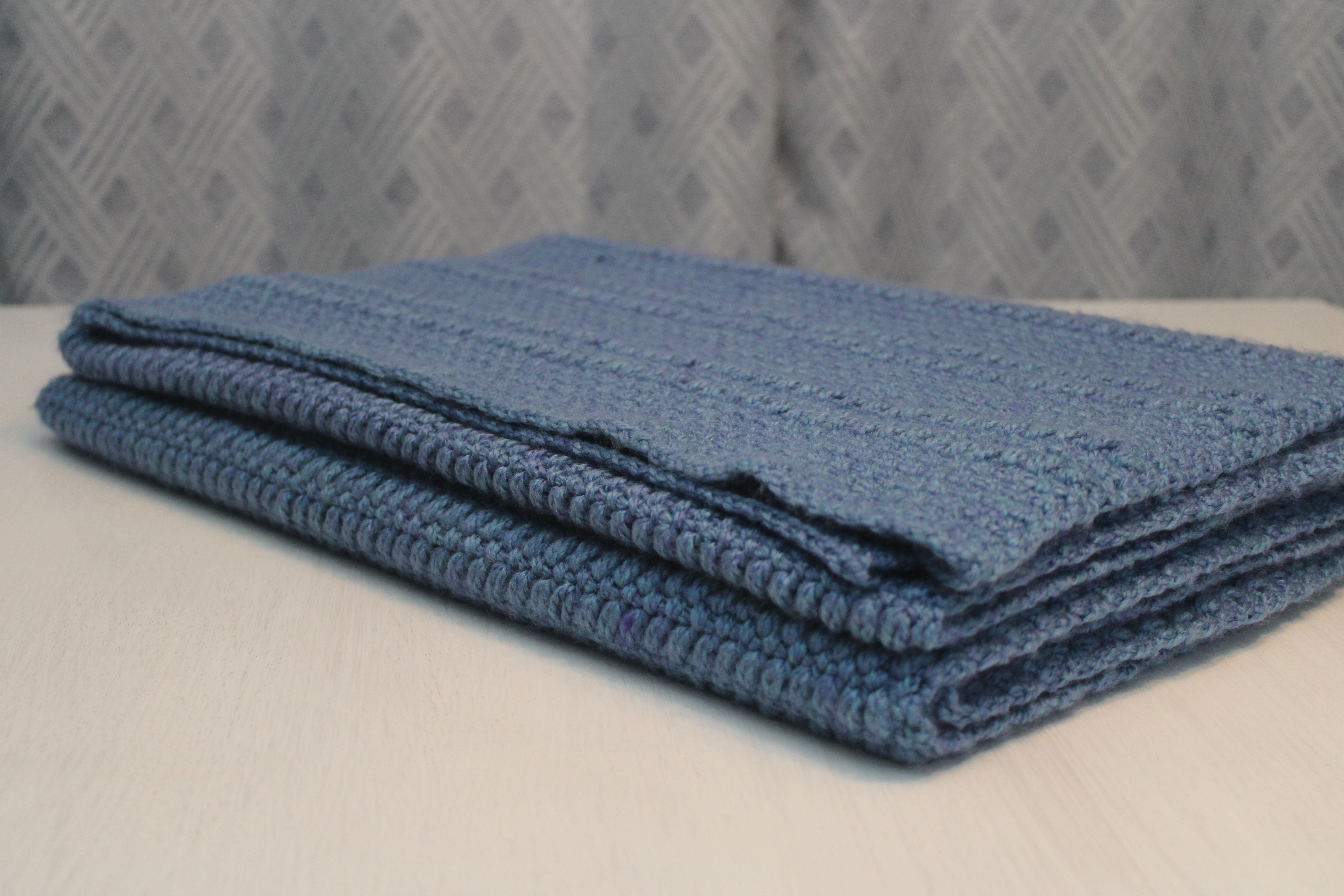 blue crocheted moss and puff stitch bed scarf folded on a dresser