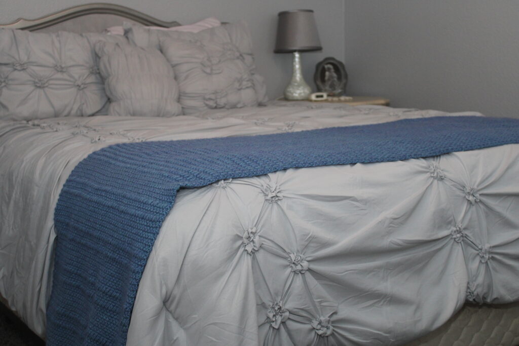 Blue crocheted moss and pff stitch bed scarf draped across foot of the bed
