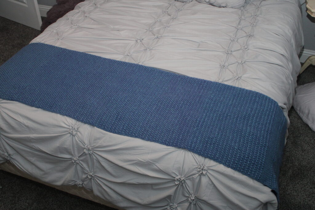blue crocheted moss and puff stitch bed scarf laid across a bed