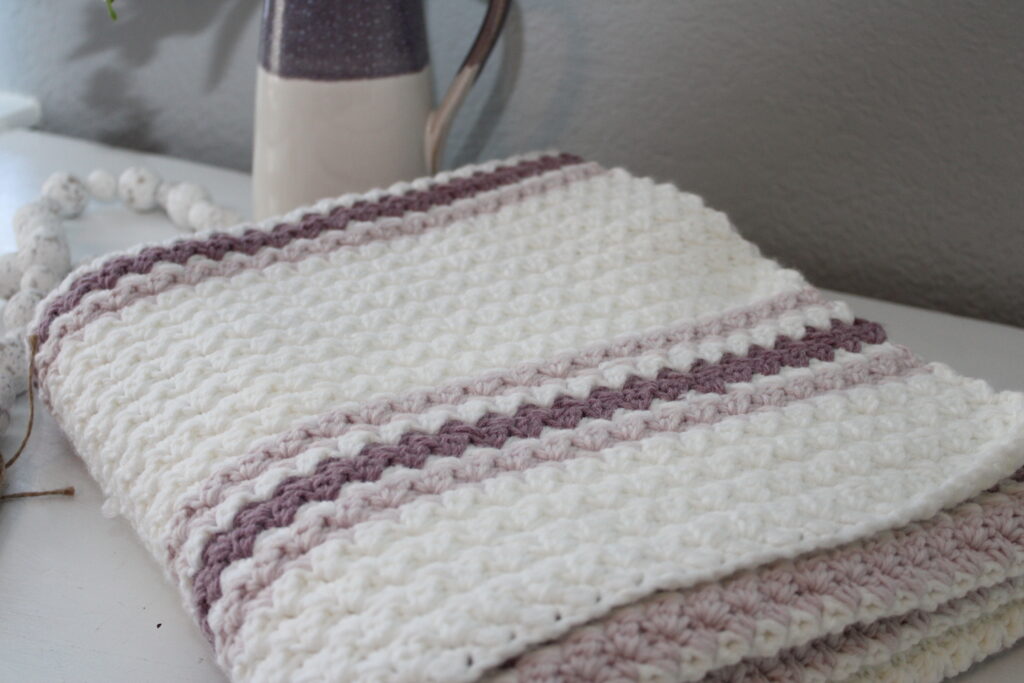 Easy Sugarplum Princess baby afghan in white with pink stirpes crocheted blanket folded on a dresser
