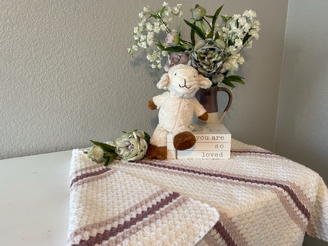 Easy Sugarplum princess baby afghan draped over dress with bunny, flower and stacked books.