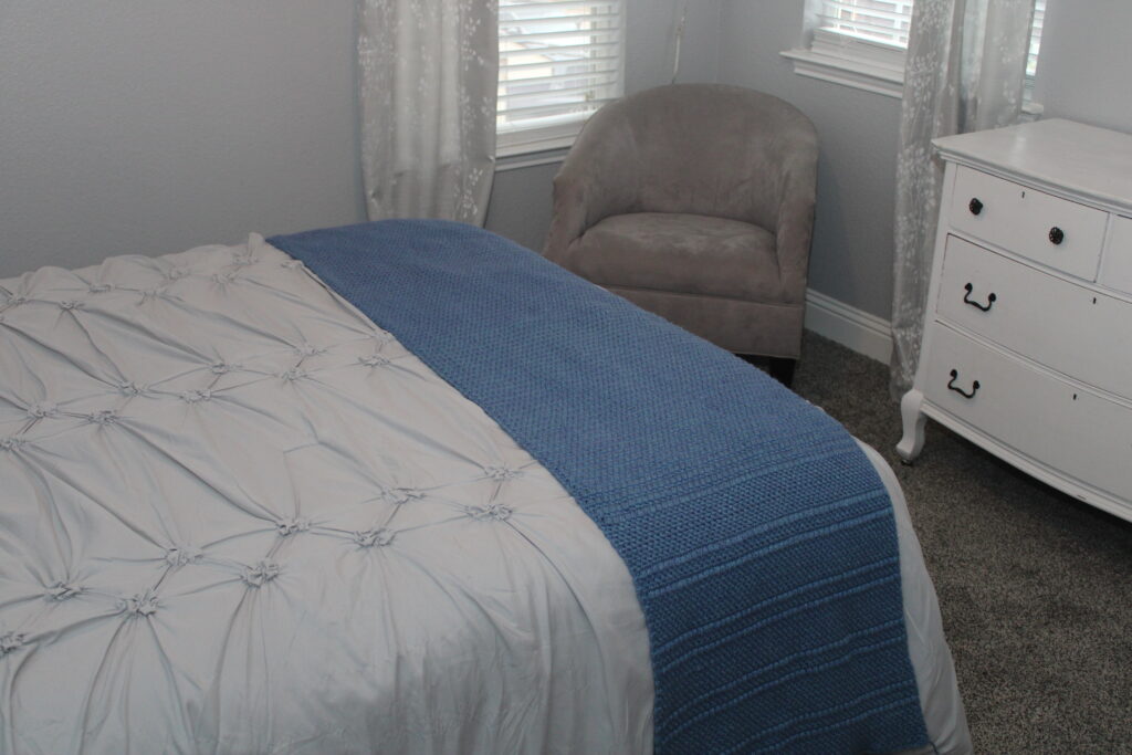 Moss and Small Puff Bed Scarf in Blue draped across a the foot of a bed.