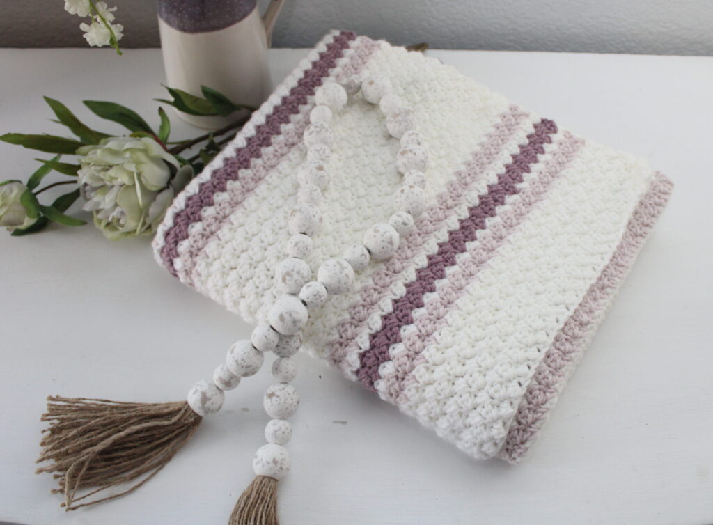 Easy Sugarplum Princess Baby afghan folded and on a dresser in purple, pink, and white
