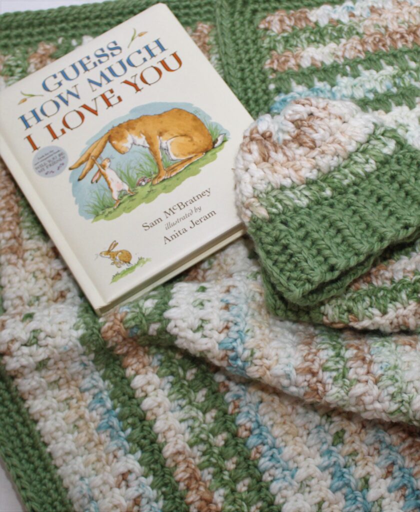 warm Woodlands themed baby blanket in green, ivory, and blue gathered with a book
